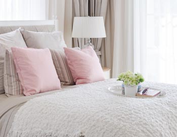 Pink,Pillows,On,Bed,With,White,Tray,Of,Flower,At